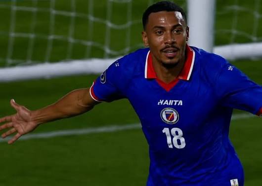 Un joueur portant le maillot numéro 18 d'Haïti, les bras écartés sur le terrain